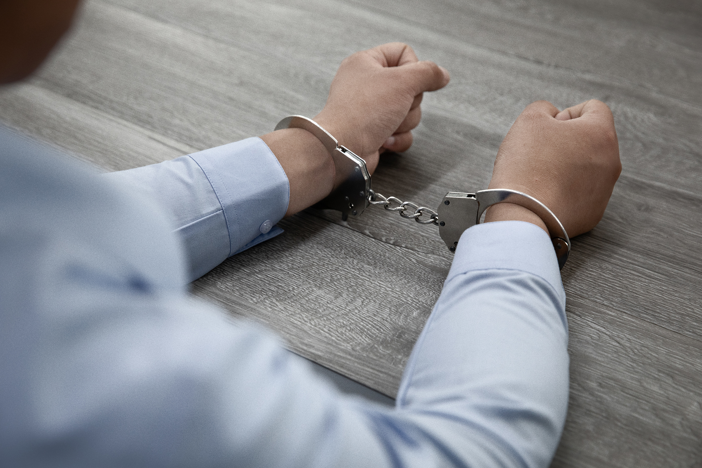 Selective focus shot male hands handcuffs wooden table